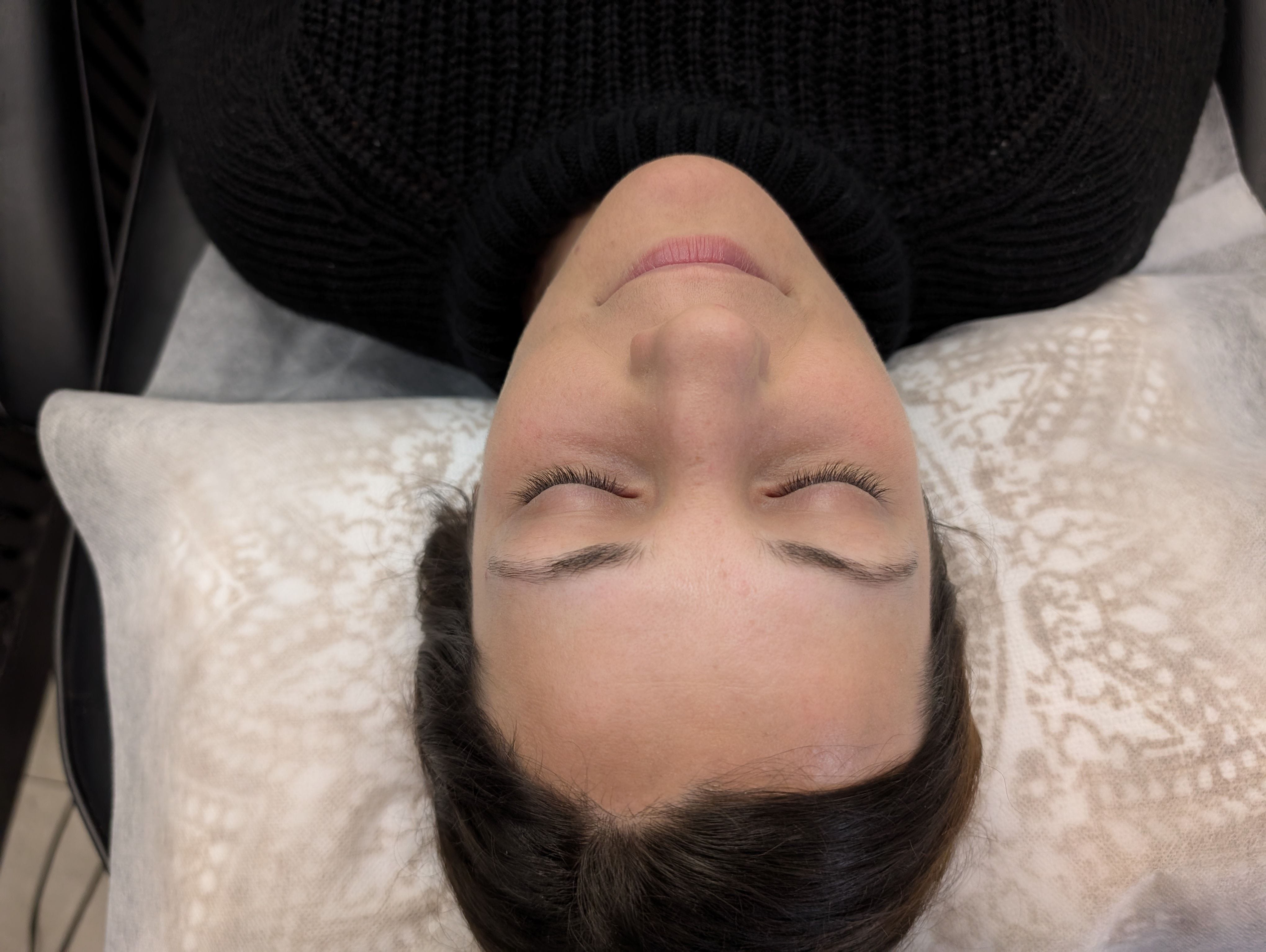 A woman smiling before she receives her eyebrow tattoo.