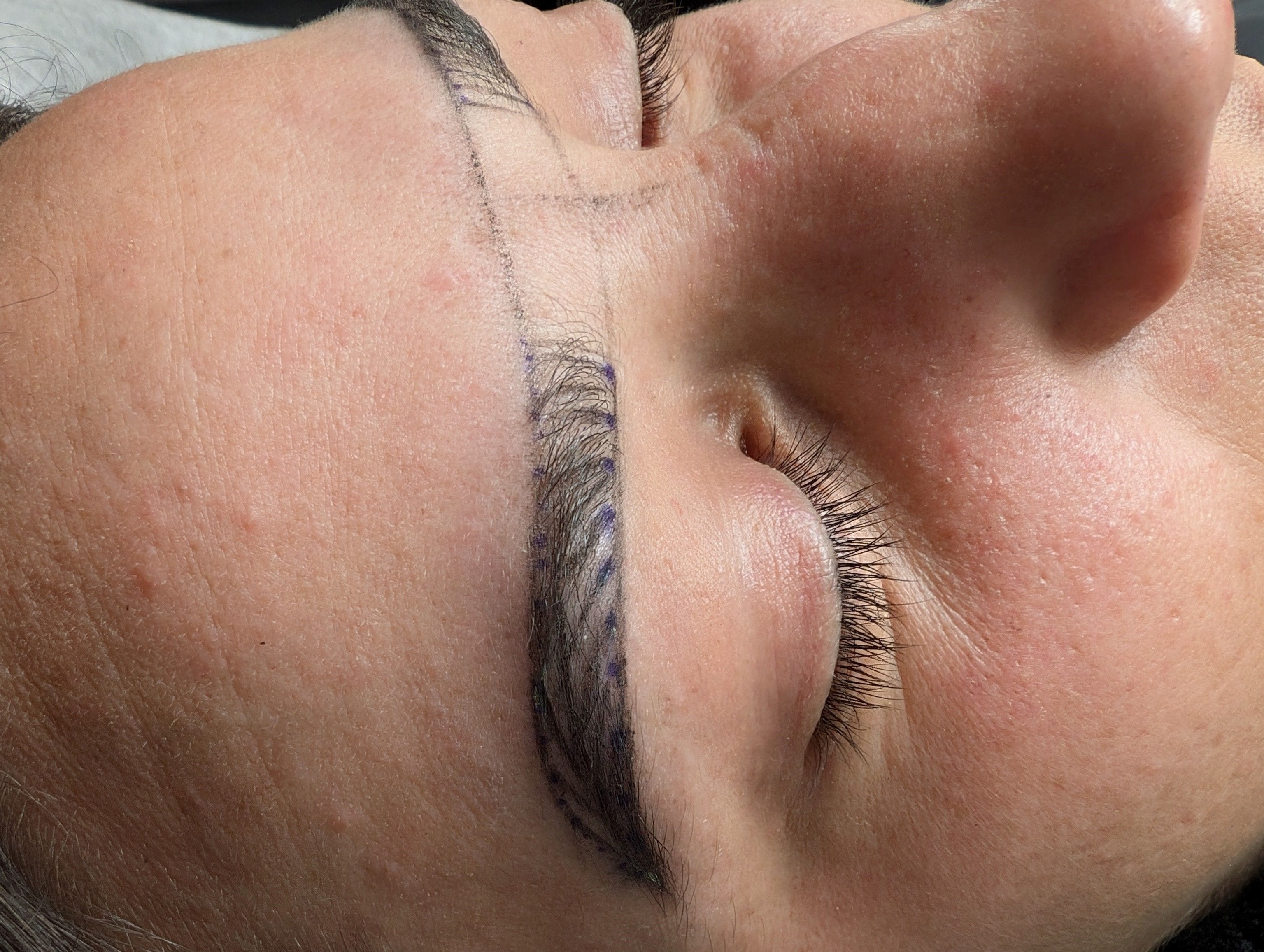 A closeup image of a woman with guidelines for the tattoo drawn on her eyebrows.