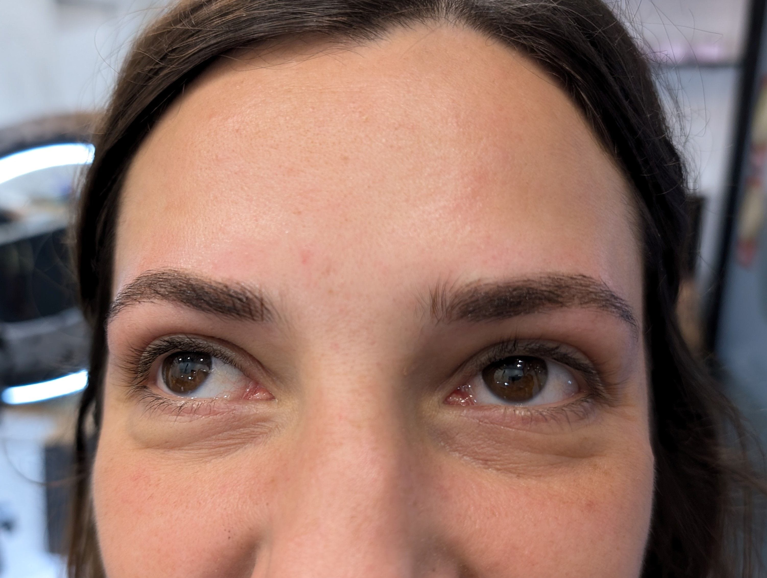 A closeup image of a woman showing the finished product of her new permanent eyebrow tattoos.