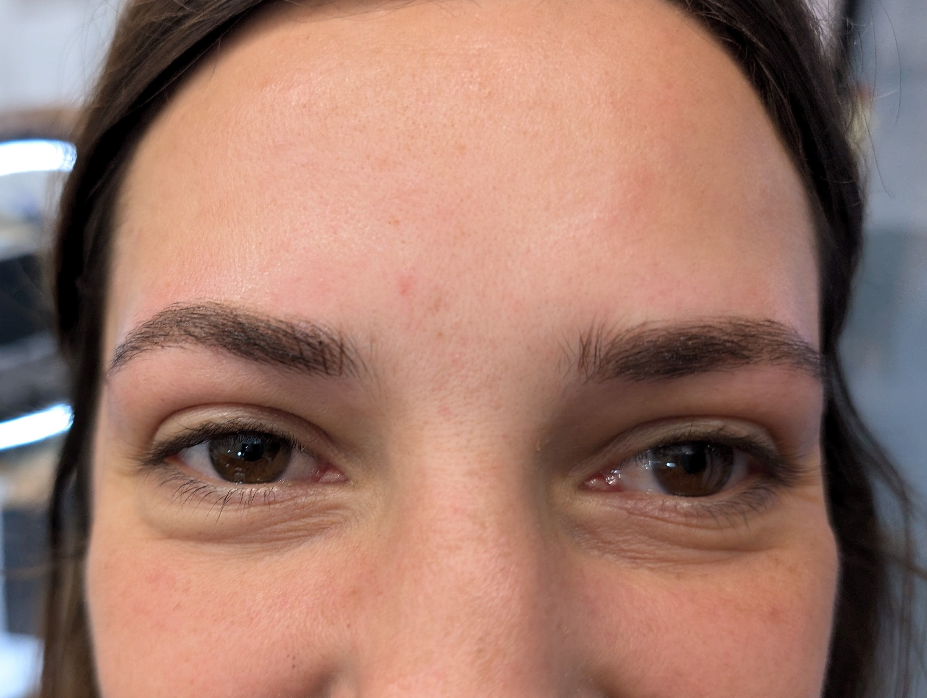 A closeup image of a smiling woman very happy with her eyebrow tattoos.